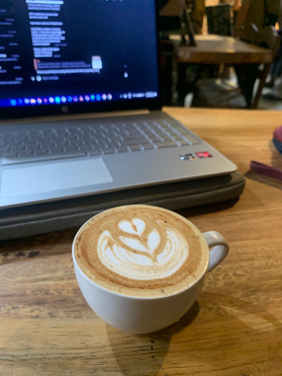 A latte beside an open laptop on a wooden café table