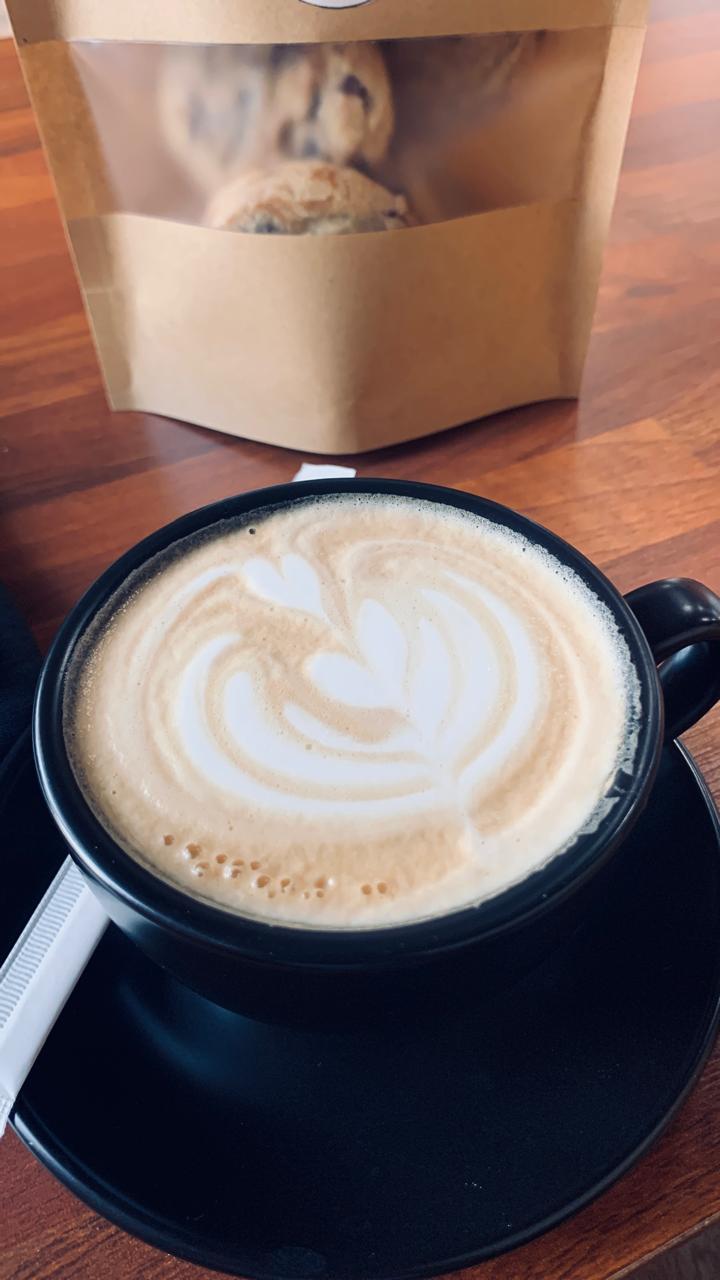 A latte with leaf art in a black cup on a wooden café table in Baguio